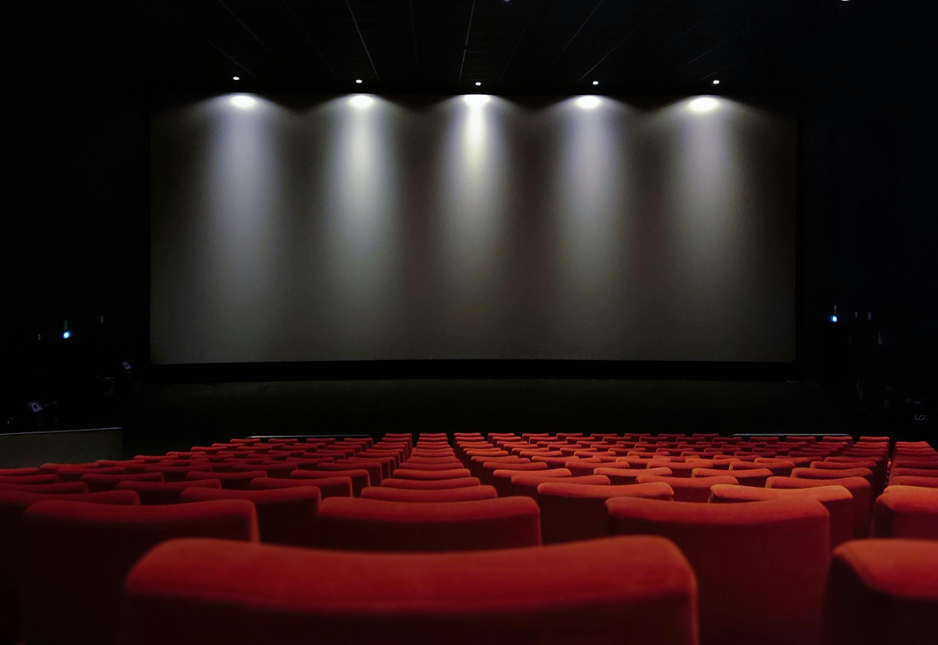 Dimly lit cinema with rows of red seats facing the screen (Pexels License)