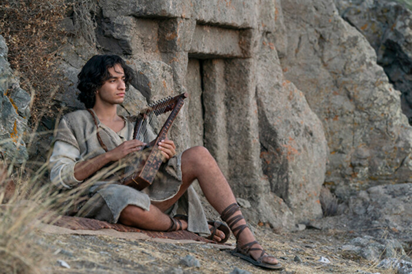 Young David sitting with harp against stone wall